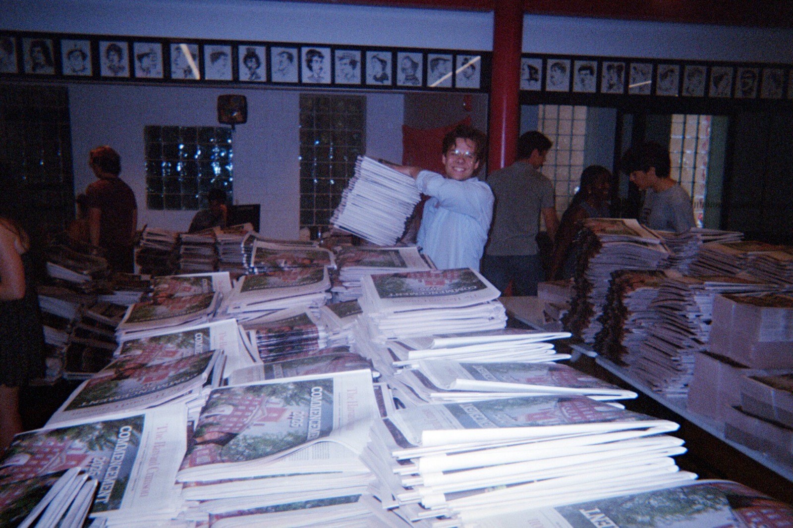 An editor holding up a stack of freshly printed Commencement issues in the newsroom